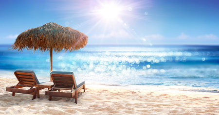 Chairs Under Parasol In Sand Beach With Abstract Defocused Bokeh Lights On Oceanの写真素材