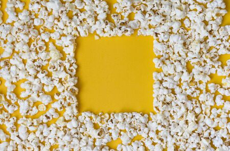 Border of popcorn scattered over yellow background with copy space, top view. Minimalistic design for movie poster, entertainment concept. Close-Up Of Popcorn Against Yellow Background. Popcorn pattern on yellow.の写真素材
