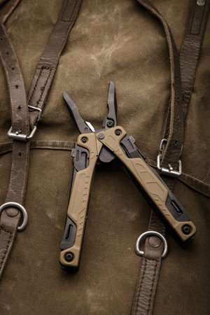 Modern multitool with many tools. A portable multitasking tool on a vintage canvas backpack. dark background.の写真素材