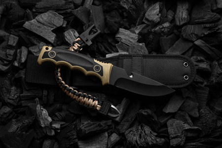 Modern knife with black blade. Hunting, military knife on smoldering charcoal. Black background.