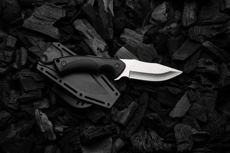 Modern knife with silver blade. Hunting, military knife on smoldering charcoal. Black background.