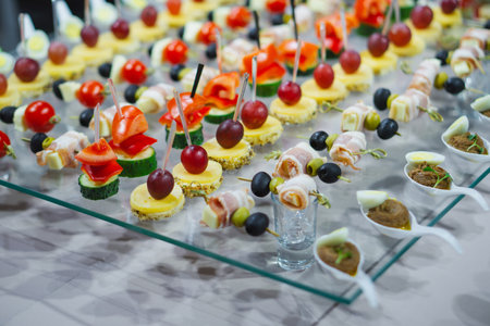 A variety of snacks and canapes are laid out on a glass table. Wickedly designed and laid out food. holiday catering. light background.の写真素材