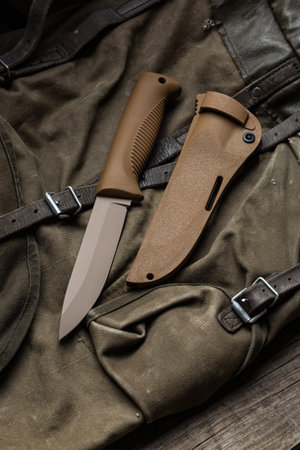 Modern knife with rubberized handle and plastic sheath. Cold steel lies on a vintage hiking...