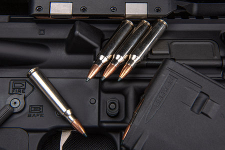 Close-up of .223 carbine cartridges. Loaded weapon clip. Weapons in the background.