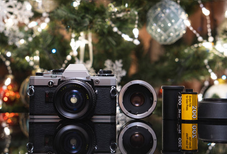 Vintage film camera with a lens and film rolls, set against a festive background with Christmas lights, reflecting on a black surface, evoking nostalgia and classic photography vibesの写真素材