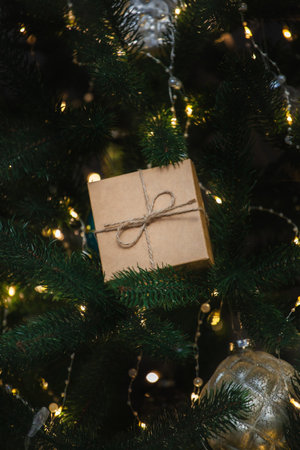 A beautifully wrapped gift box with twine is nestled among the branches of a decorated Christmas tree, adorned with twinkling lights and ornaments, creating a festive holiday atmosphere.の写真素材