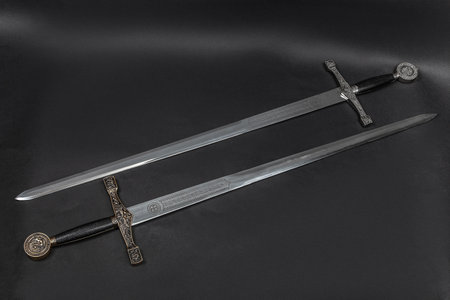 Two historical decorative longswords or greatswords on a dark, textured surface.