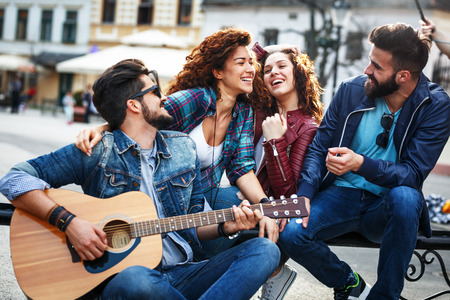 Group of friends hangout on street in city downtown.They standing by the city square,drinking and playing guitar.の写真素材