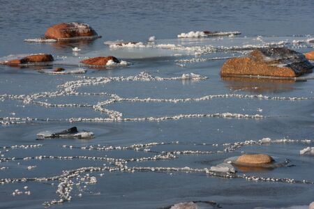Stones and Ice Patterns in Snow on Seaside in Sunny Dayの写真素材