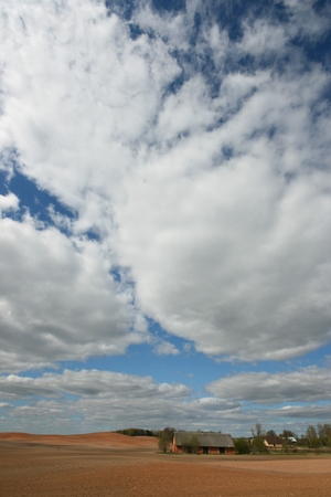Country house in plough-land under cloudy sky in springの写真素材