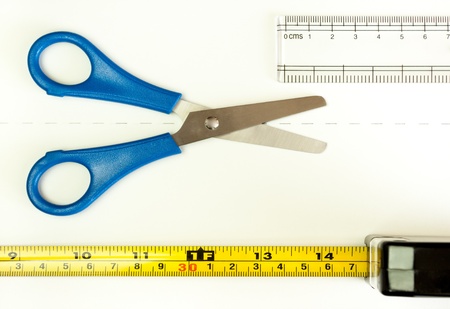 The  Measure Twice, Cut Once  proverb illustrated by a ruler and a tape measure for the two measurements and a pair of scissors ready to cut along the line marked on the white sheet の写真素材