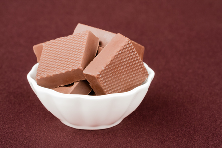 Chocolate Squares In A Bowl - Chocolate squares in a white bowl on maroon background.の写真素材