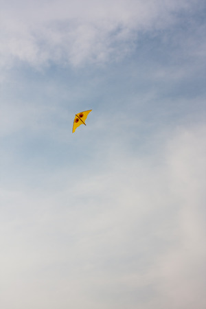 Kite flying against blue sky - An yellow kite being flown in the wind against blue sky.の写真素材