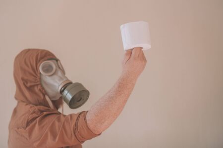 Man in a gas mask holds a roll of toilet paper. Concept: lack of toilet paper in supermarkets and local stores, the last roll of toilet paper in a shop.の写真素材