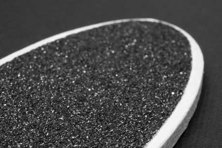 Pumice stone for feet on a wooden handle on a black background close-up. Macrophotography.