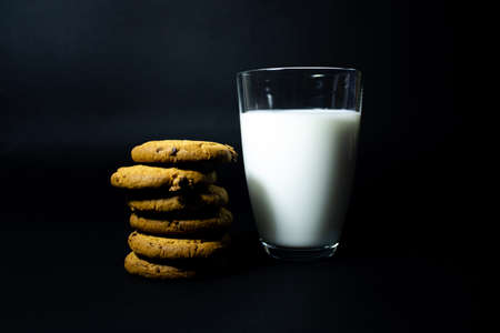 A glass of milk and oatmeal cookies with raisins on a black background.の写真素材