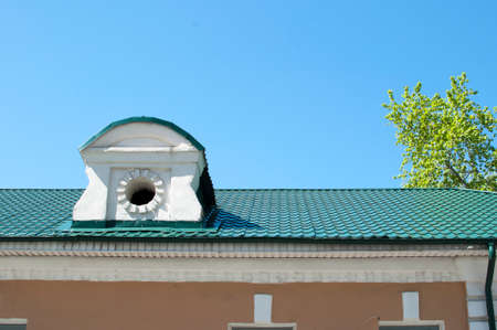 The roof of an old house with a dormer window. Close-up of a green tiled roof. Background of blue...