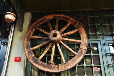 A large wooden wheel from a cart on the window. Decorative element on a window with a metal grill.のeditorial素材