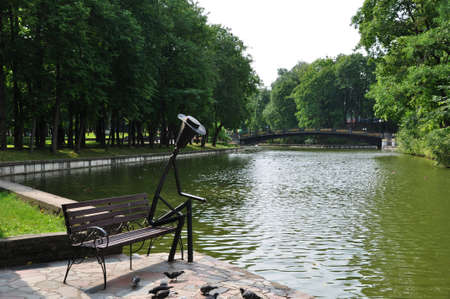 Panorama of the city pond. Bench with a figurine of a man sitting on it. 02 August 2021, Smolensk, Russia.のeditorial素材