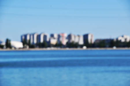 Defocused and blurred background of high-rise buildings in the city. View of the wide river and coastline with houses.の写真素材