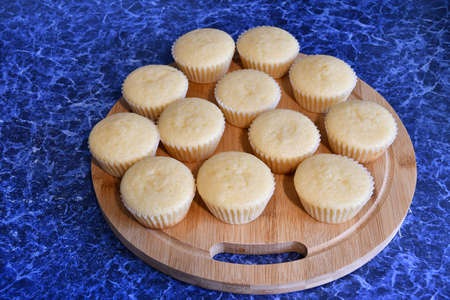 Fresh cupcakes in paper form on a wooden round board. Board with cupcakes on a blue table top.の写真素材
