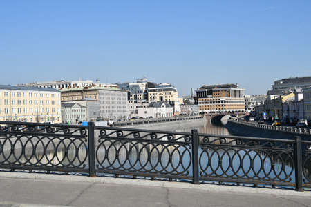 Panoramic view of the cast-iron parapet of the bridge through the drainage channel. View of the stone buildings on the embankment. March 24, 2022 Moscow, Russia.のeditorial素材