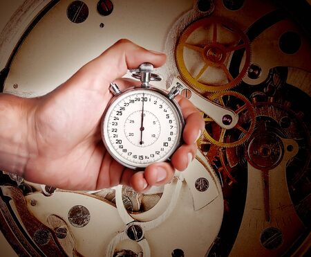 Stopwatch in man's hand on dark background of old watch mechanism