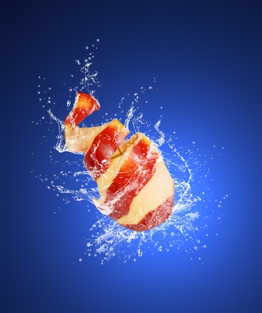 Red apple with the skin peeled like a spiral in water splashes on the dark blue backgroundの写真素材