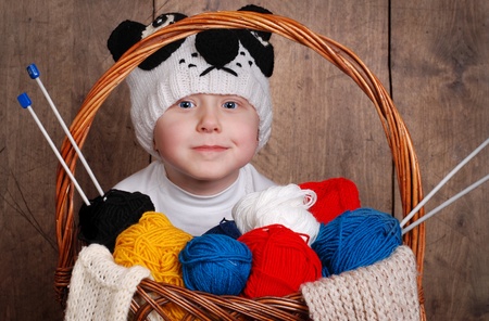 Little boy in knitting panda hat with wool yarn into basketの写真素材