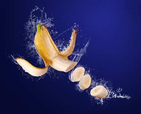 Yellow banana with peeled  skin and sliced pieces  in water splashes on the dark blue backgroundの写真素材