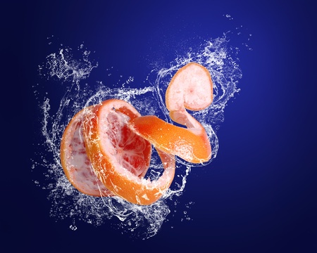Red grapefruit with skin  peeled like a spiral in water splashes on the dark blue backgroundの写真素材