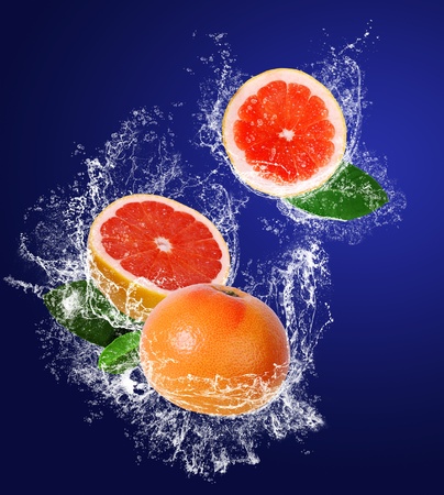 Red guicy grapefruits with leaves in water splahes on the dark blue backgroundの写真素材
