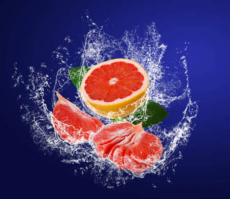 Red guicy segments of grapefruits with leaves in water splahes on the dark blue backgroundの写真素材