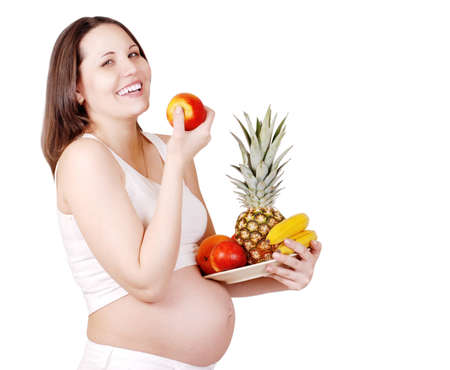 Happy smiling pregnant woman with plate of fruits over white backgroundの写真素材