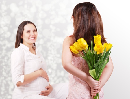Little daughter has bouquet of yellow tulips like surprise for her pregnant motherの写真素材