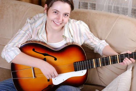 Smiling teenage girl playing by guitar sitting on the sofa at homeの写真素材