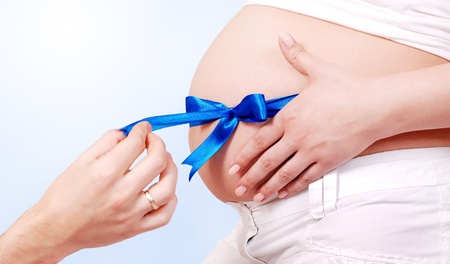 Pregnant tummy with blue ribbon and man handの写真素材