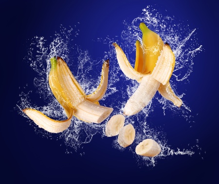 Two Yellow bananas with the peeled  skin  in water splashes on the dark blue backgroundの写真素材