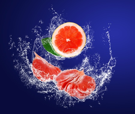 Red guicy pieces of grapefruits with leaves in water splahes on the dark blue backgroundの写真素材