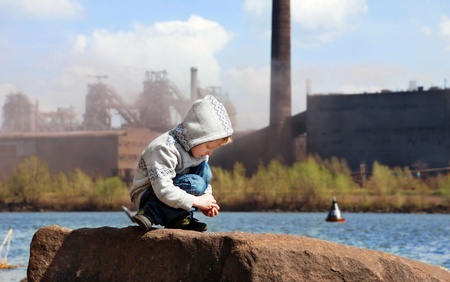 Playing little boy on the river coast in front of metallurgy factoryの写真素材