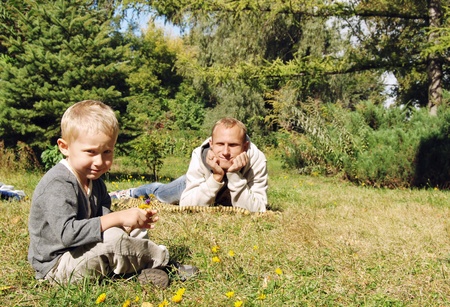 Son and father relax on the green lawn at the parkの写真素材