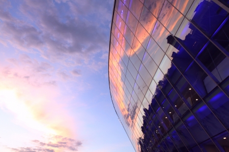 Modern glass building with reflected evening city and sunset sky in itの写真素材