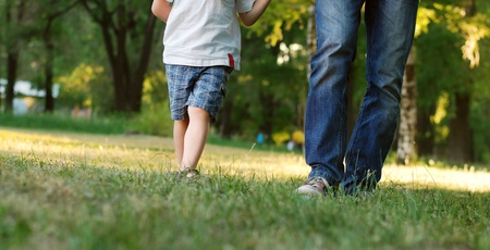 Father and son legs walk across green lawn in the parkの写真素材