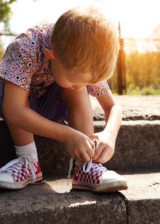 Boy tying the laces on sneakers sitting on the stepsの写真素材
