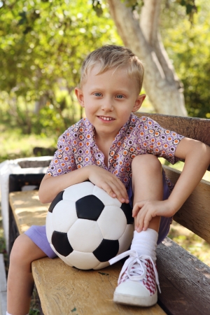 Cute boy with ball sitting on the bench at the parkの写真素材