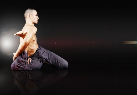 Yong man doing yoga exercise on black mirrored backgroundの写真素材