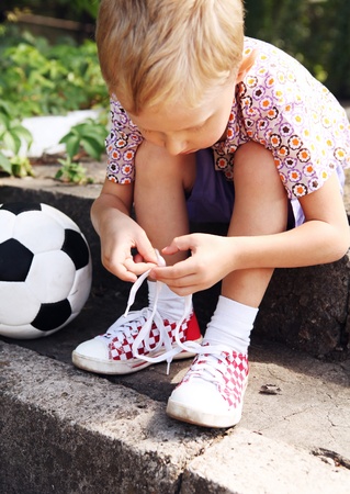 Boy trying to tie lace on his sneakers sitting on the stepsの写真素材