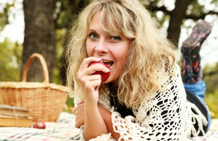 Happy young woman eating red apple on autumn picnicの写真素材