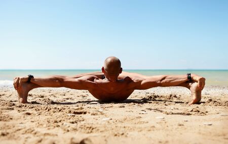 Yoga practice. Man in strong stretching yoga pose on the sea beachの写真素材