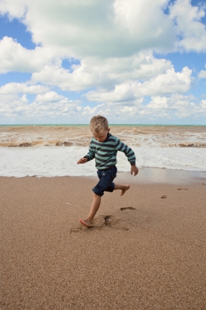 Shoeless happy little boy running at the sea coastの写真素材